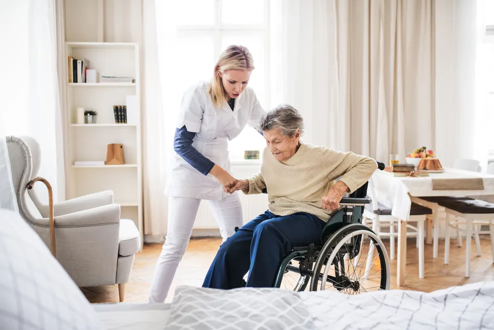 A caregiver helps an older woman rise from her wheelchair.
