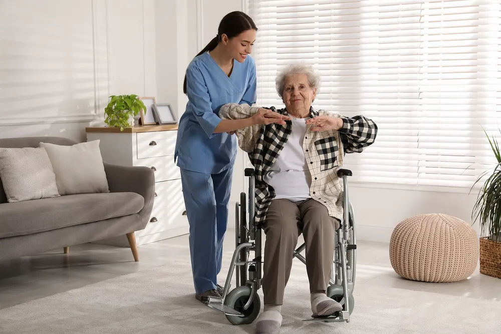 A caregiver helps an older woman in a wheelchair at home.